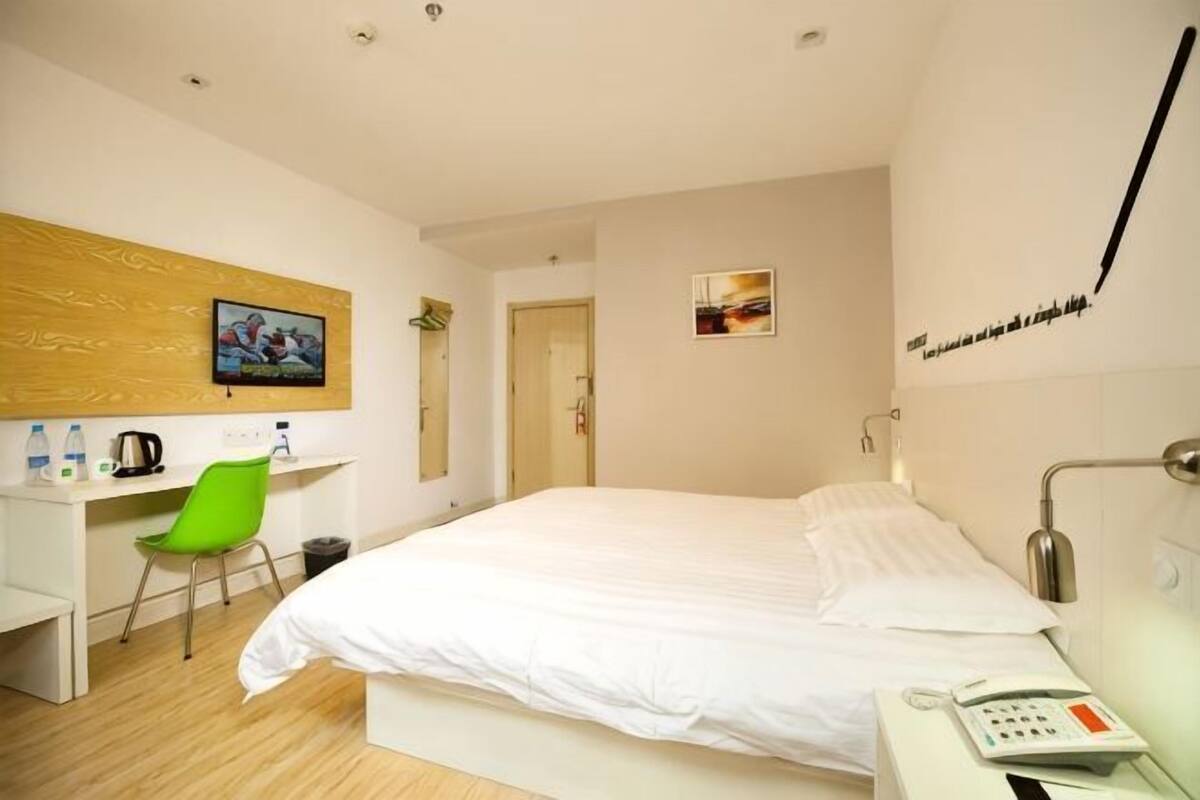 A hotel room with a bed, a desk, a chair, a telephone, and a wall-mounted TV.