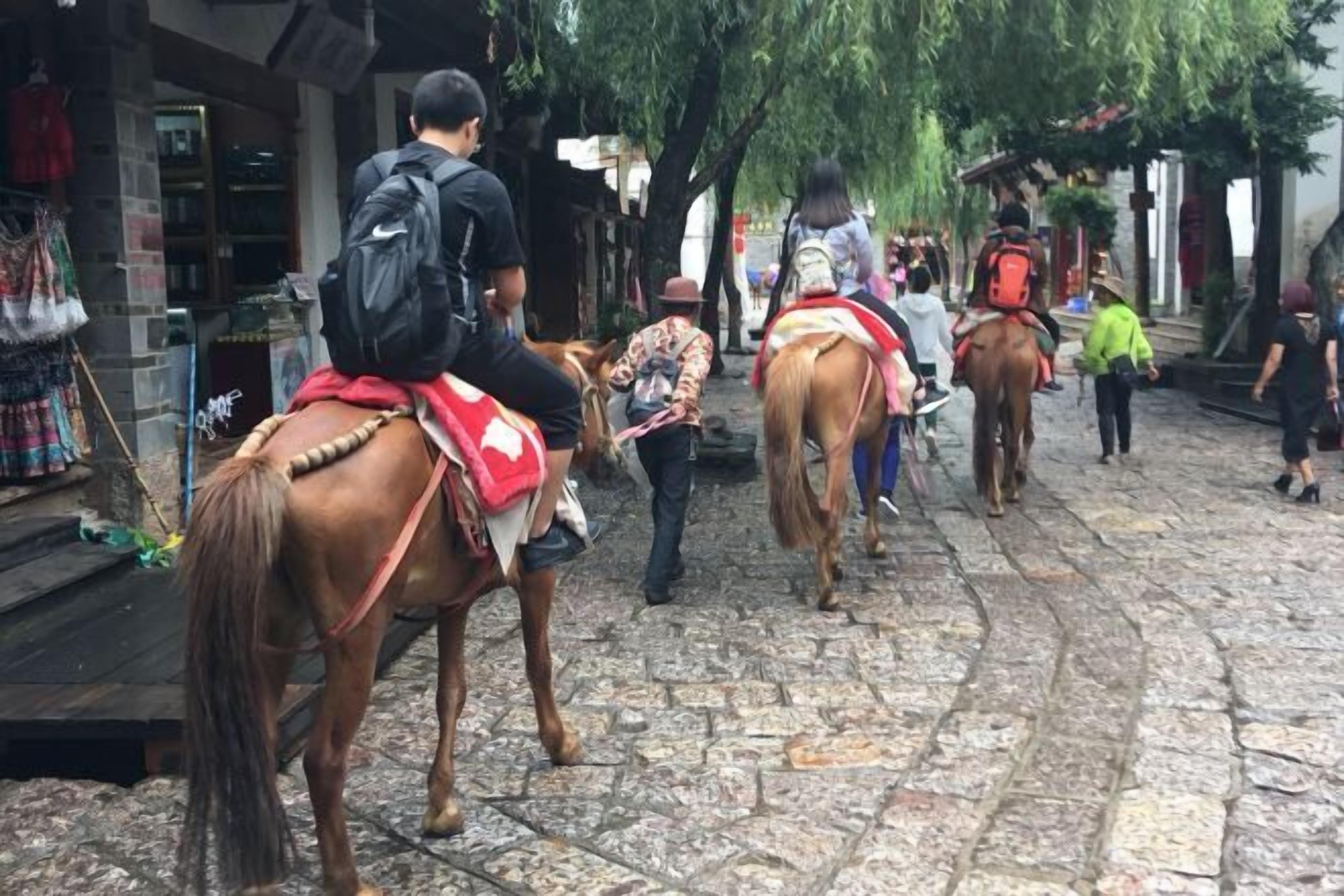 A cobblestone street with people riding horses.