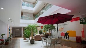 A spacious indoor area with a high ceiling, a red umbrella, potted plants, a sofa, and a wall with a cartoon character. - Motel Lijiang Xueshan Road (Lijiang)