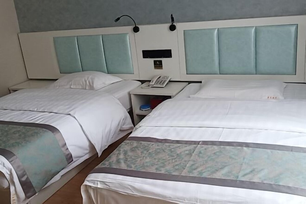 A hotel room with two single beds, a bedside table with a phone, and a small shelf with a bottle.