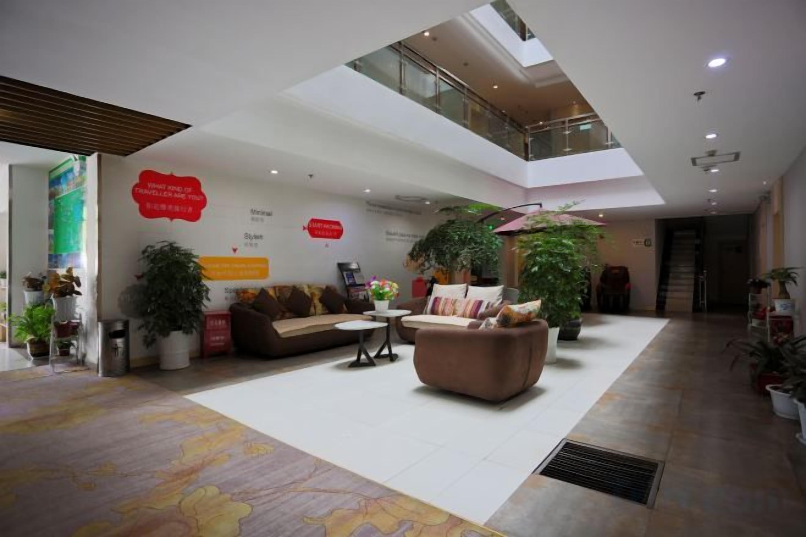 Un hall d’entrée spacieux avec un plafond haut, un espace salon central et de nombreuses plantes en pot.