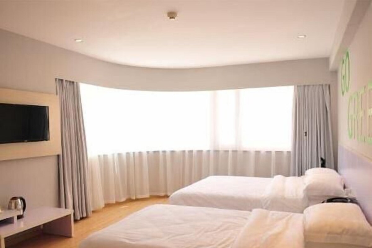 A hotel room with two beds, a TV on the wall, and a window with curtains.