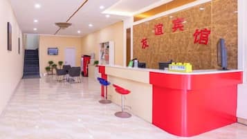 A reception area with a red counter, a TV, and a staircase in the background.