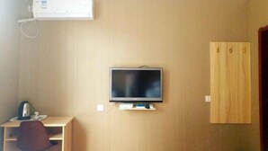 A room with a mounted television, a desk with a chair, and a wooden wardrobe.