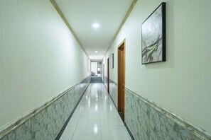 Un long couloir étroit, doté d’un sol en marbre, avec une porte en bois au bout et un tableau encadré accroché au mur.