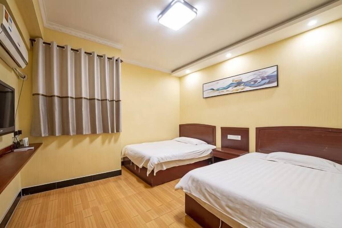 Een hotelkamer met twee enkele bedden, een bureau met stoel, een flatscreen televisie, een raam met gordijnen en een schilderij aan de muur.
