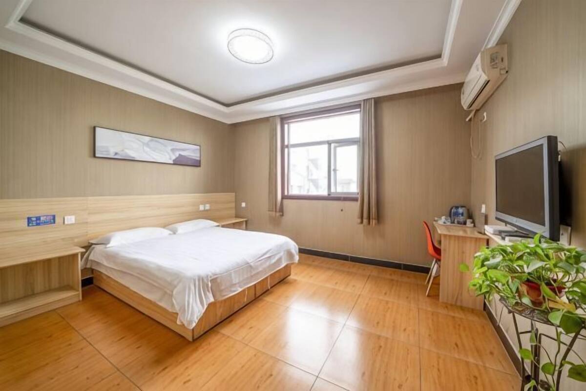 Een hotelkamer met een bed, een bureau met een televisie, een raam en een plant.