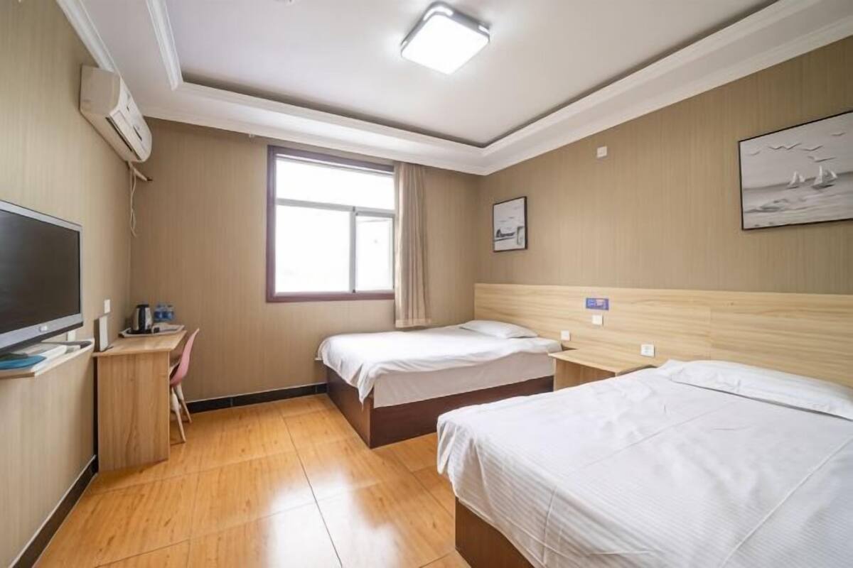 Een hotelkamer met twee bedden, een bureau, een televisie en een raam.
