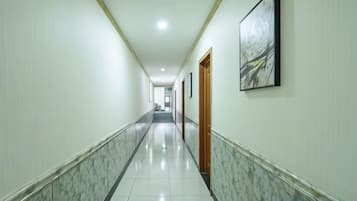 A long, narrow hallway with a marble floor, wooden doors, and framed artwork on the walls.