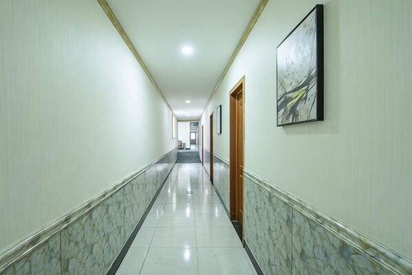 A long, narrow hallway with a marble floor, wooden doors, and framed artwork on the walls.