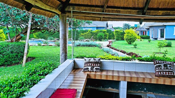 Un espace extérieur abrité, aménagé avec des sièges, offrant une vue sur un jardin bien entretenu et une maison bleue en arrière-plan.