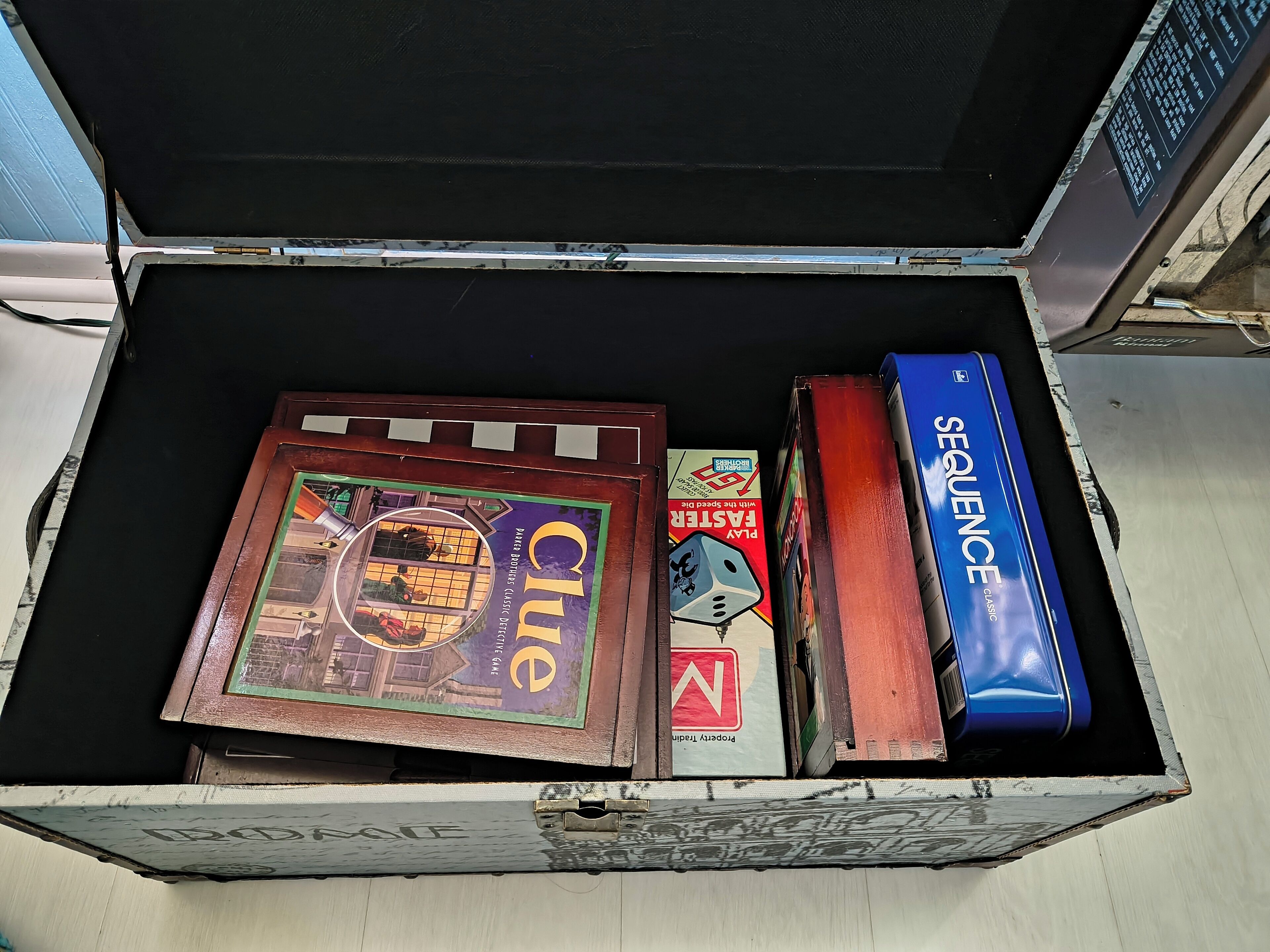 Una caja con juegos de mesa, incluyendo Clue, Monopoly y Sequence.