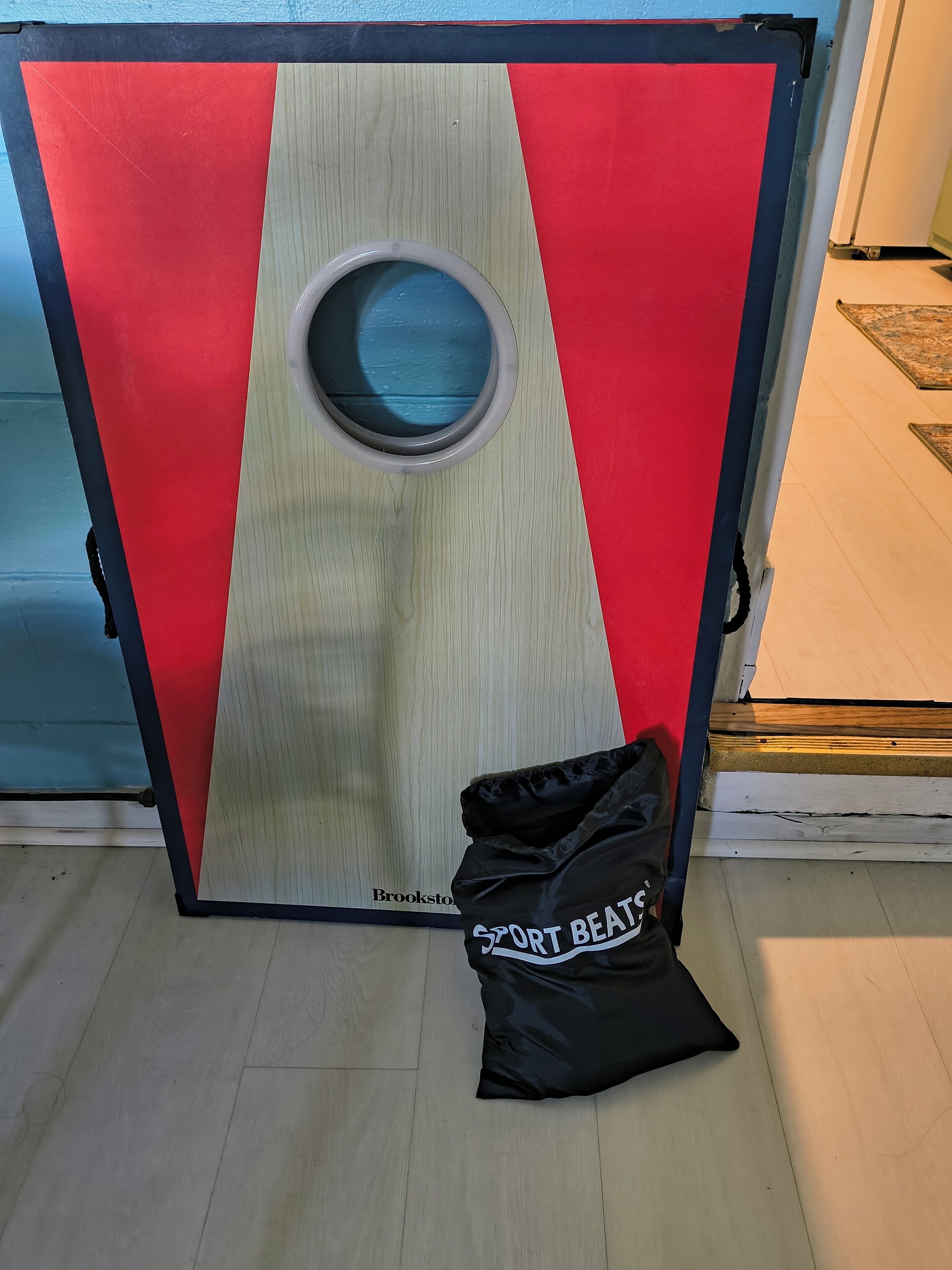 A room with a door featuring a red and beige color scheme, a circular window, and a black bag labeled 'SPORT BEATS' on the floor.