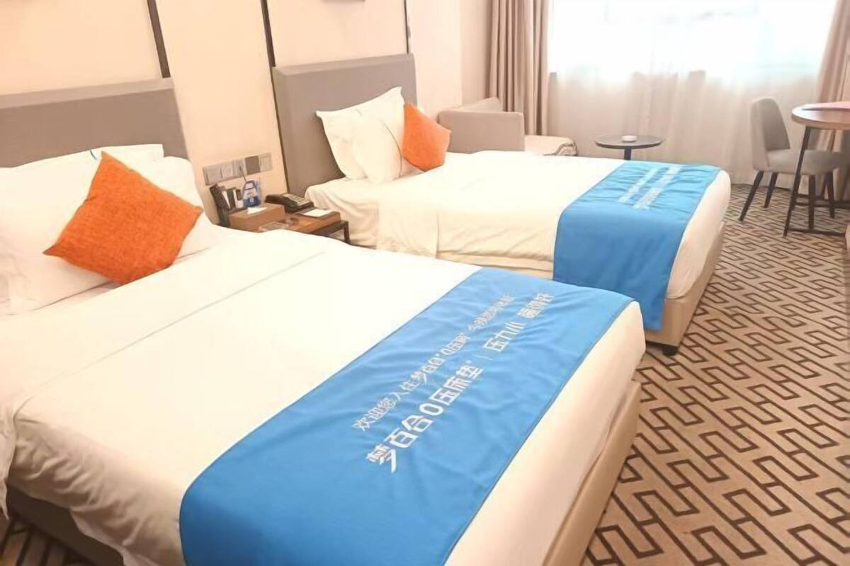Dos llits d'hotel amb llençols blaus, una taula petita i una cadira.