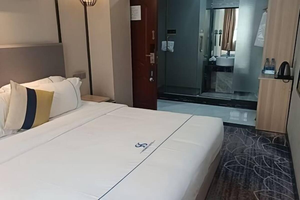 Habitació d'hotel amb un llit, una tauleta de nit, una porta que dona a un bany i un terra amb moqueta.