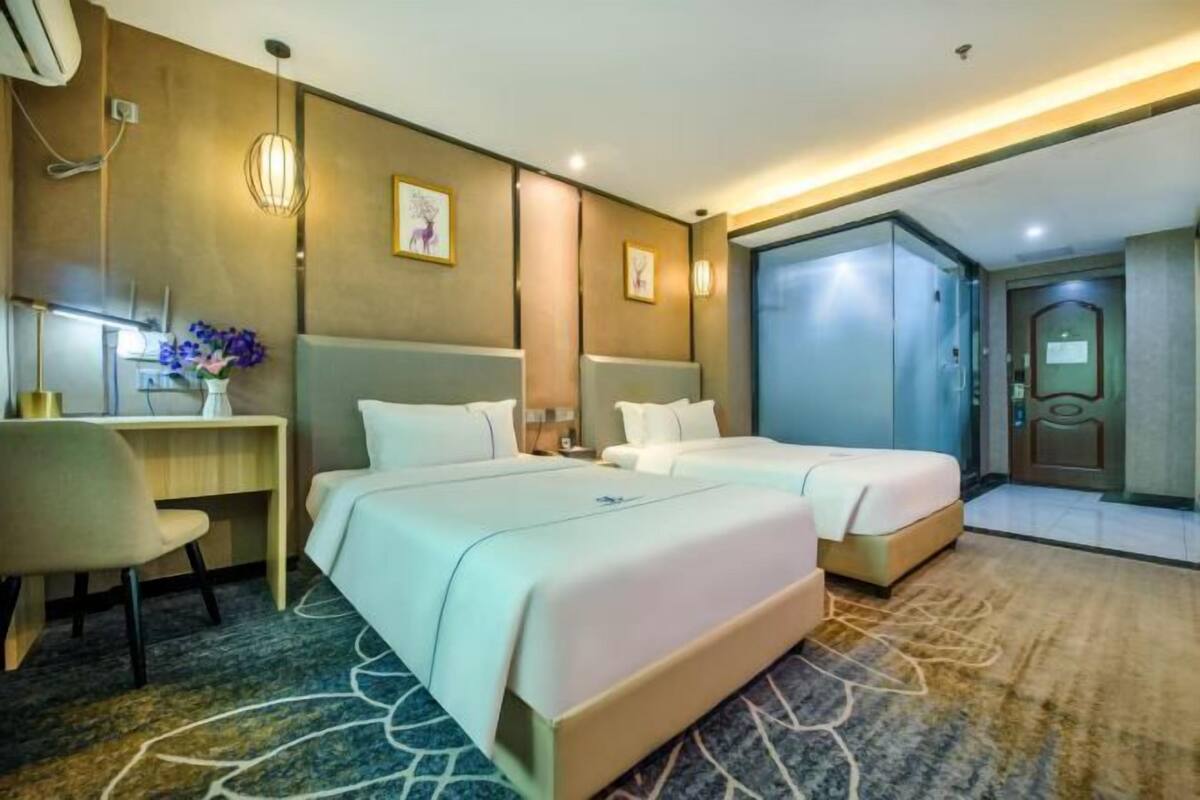 Habitació d'hotel amb dos llits, una taula de treball, una cadira, un armari i un bany.