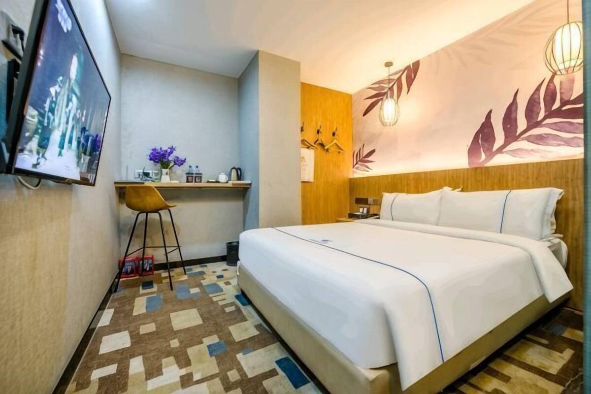 Habitació d'hotel amb un llit, escriptori, cadira, televisor i paret amb un dibuix de fulles.