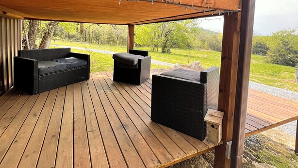 Une terrasse en bois avec des sièges d’extérieur, une rambarde en bois et une vue sur le paysage environnant.