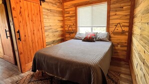 Une chambre dans une cabane en bois, avec un lit, une fenêtre et un ventilateur de plafond.