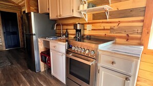 Une cuisine compacte aux murs en bois, dotée d’un four encastré, d’un réfrigérateur et d’une machine à café.