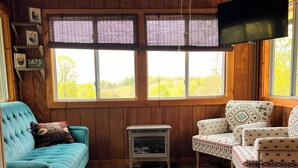 L’intérieur chaleureux d’un chalet avec un canapé bleu, des fauteuils à motifs, un plancher en bois, un tapis en peau de vache et une radio d’époque.