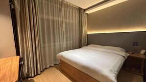 A hotel room with a bed, a desk, a nightstand, and a curtain. - Jiahao Hotel (Changzhou)
