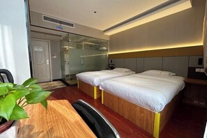 Una habitación de hotel con dos camas, un escritorio de madera, una silla y una planta en maceta.