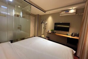 Habitació d'hotel amb llit, televisió, dutxa i una cuineta petita.