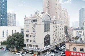 Un edificio de varios pisos con un ventanal arqueado central y una fila de coches estacionados al frente.