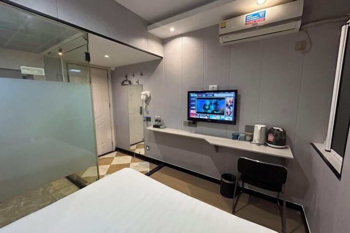 Habitació d'hotel moderna amb un llit gran, un escriptori amb un ordinador, un televisor fixat a la paret i una cadira petita.