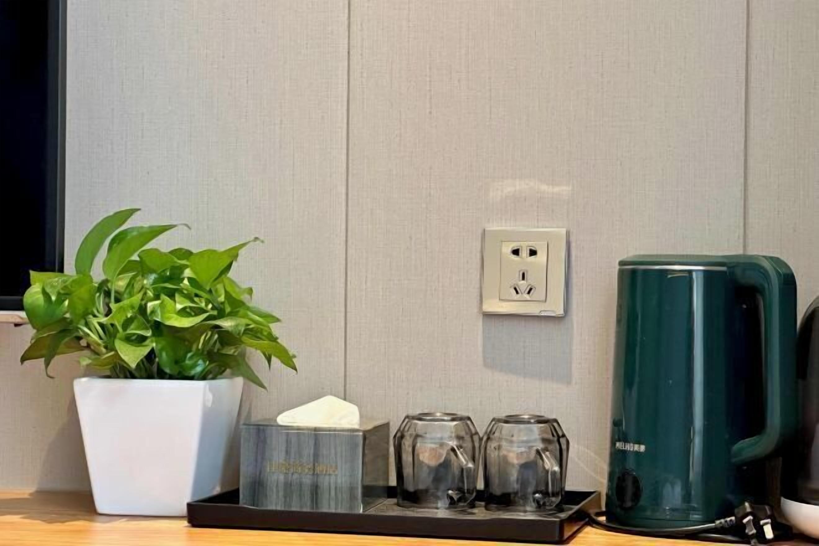 A small table with a potted plant, a tissue box, two glasses, and a green kettle.
