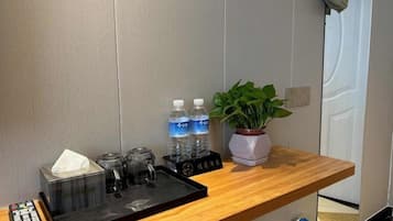 Zona de recepción de un hotel con un mostrador de madera, un control remoto, una caja de pañuelos, dos botellas de agua, una cafetera y una planta en maceta.