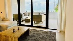 A modern living room with a sofa, coffee table, and a view of the sea through large sliding doors.