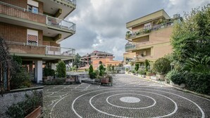 Un patio con un diseño circular de mosaico, rodeado de edificios de varios pisos con balcones y plantas en macetas.