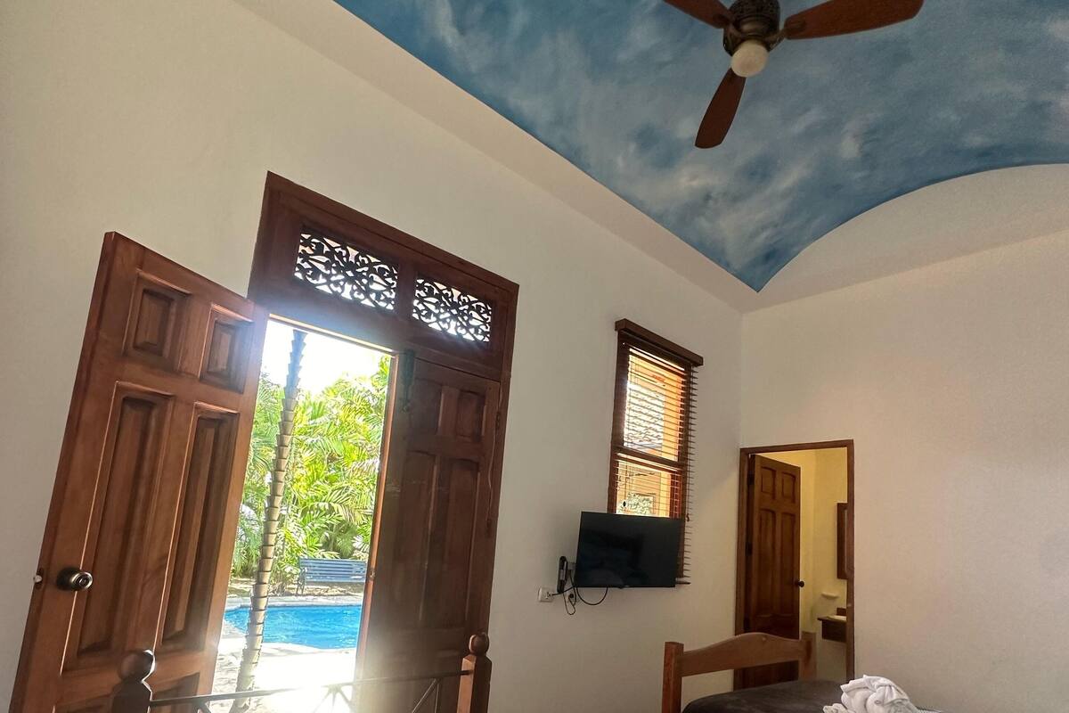 Une chambre avec deux lits, un ventilateur de plafond, une télévision et une vue sur l’extérieur.
