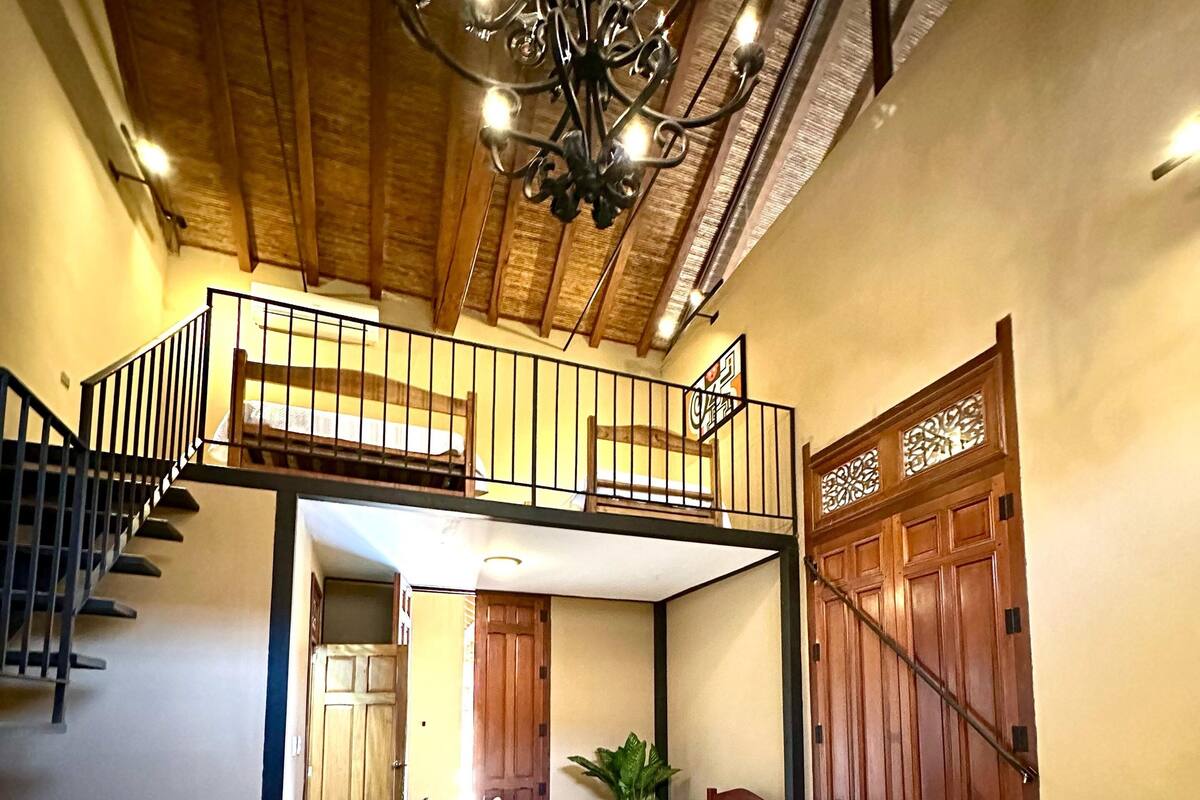 Une pièce avec un lit en mezzanine, un bureau avec un ordinateur portable et un escalier menant à un niveau supérieur.