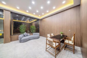 A modern room with a dining table, chairs, a sofa, and a large window with plants. - Yue'er Business Hotel (Shanghai)