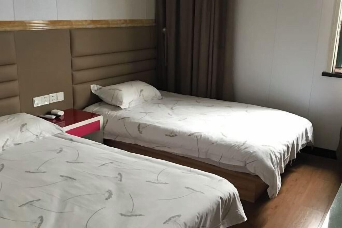 Une chambre d’hôtel avec deux lits simples, une tête de lit en bois, une table de chevet rouge et une fenêtre avec des rideaux.