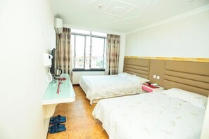 Une chambre d’hôtel avec deux lits, un bureau avec une chaise, une fenêtre avec des rideaux et une vue sur les bâtiments environnants.