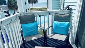 A balcony with two chairs, a table with a plate of food, and a view of the ocean. - Family-friendly, Updated Condo- Stocked Beach Closet-Steps to Crescent Beach-NMB (North Myrtle Beach)