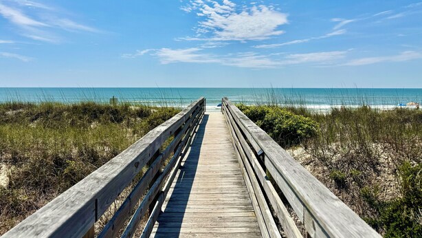 A wooden boardwalk leading to a beach with clear skies and calm waters. - Family-friendly, Updated Condo- Stocked Beach Closet-Steps to Crescent Beach-NMB (North Myrtle Beach)