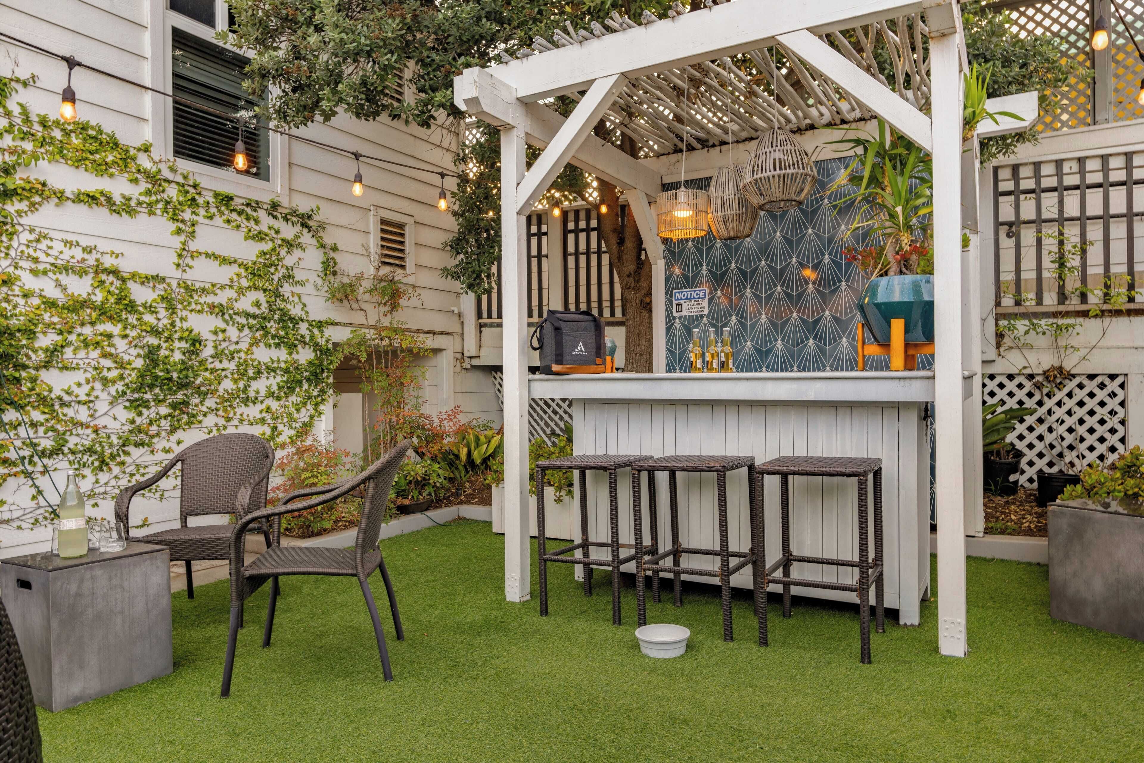 A patio area with a white pergola, a bar counter, and two wicker chairs.