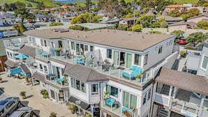 A multi-story building with balconies, outdoor seating, and a visible storefront. - 2 Cayucan Bungalows Steps to Beach + Shared Lounge Sleeps 12 (Cayucos)