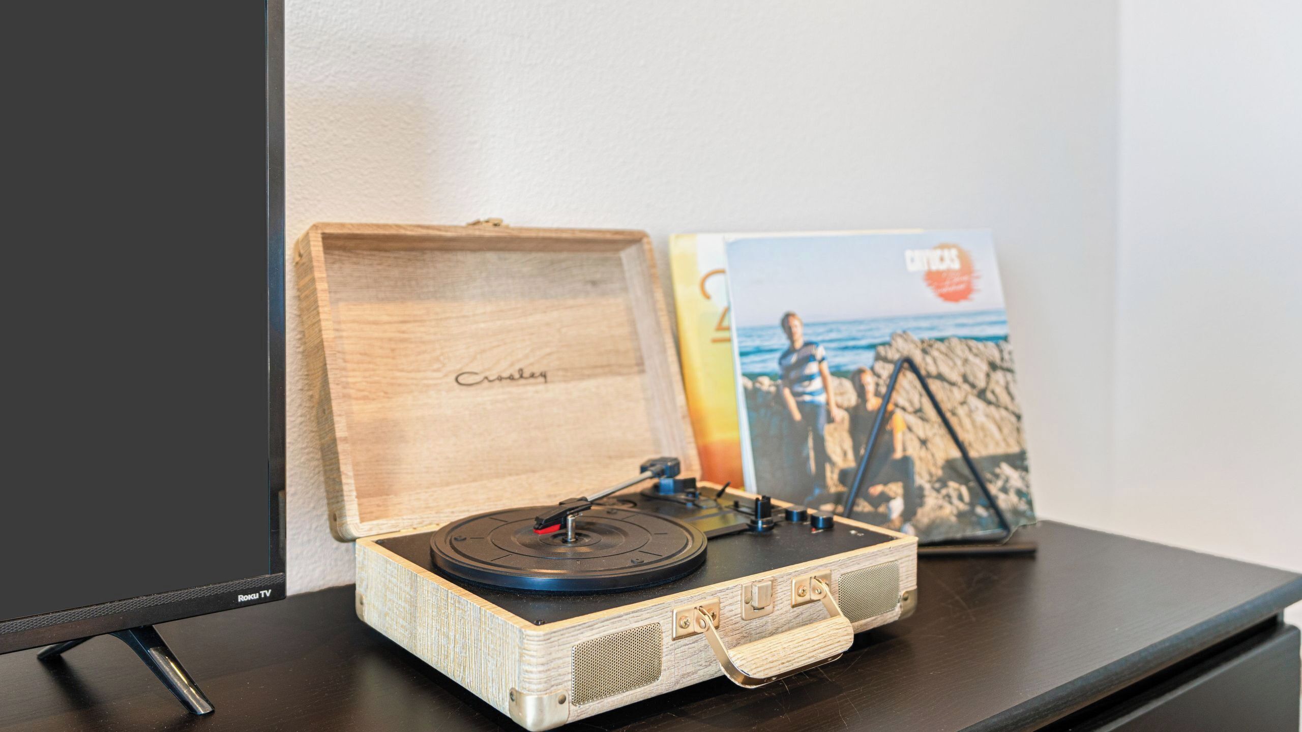 A wooden record player on a table with a book and a poster in the background.