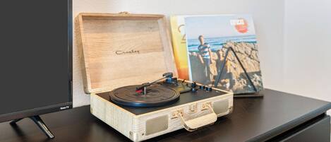 A wooden record player on a table with a book and a poster in the background.