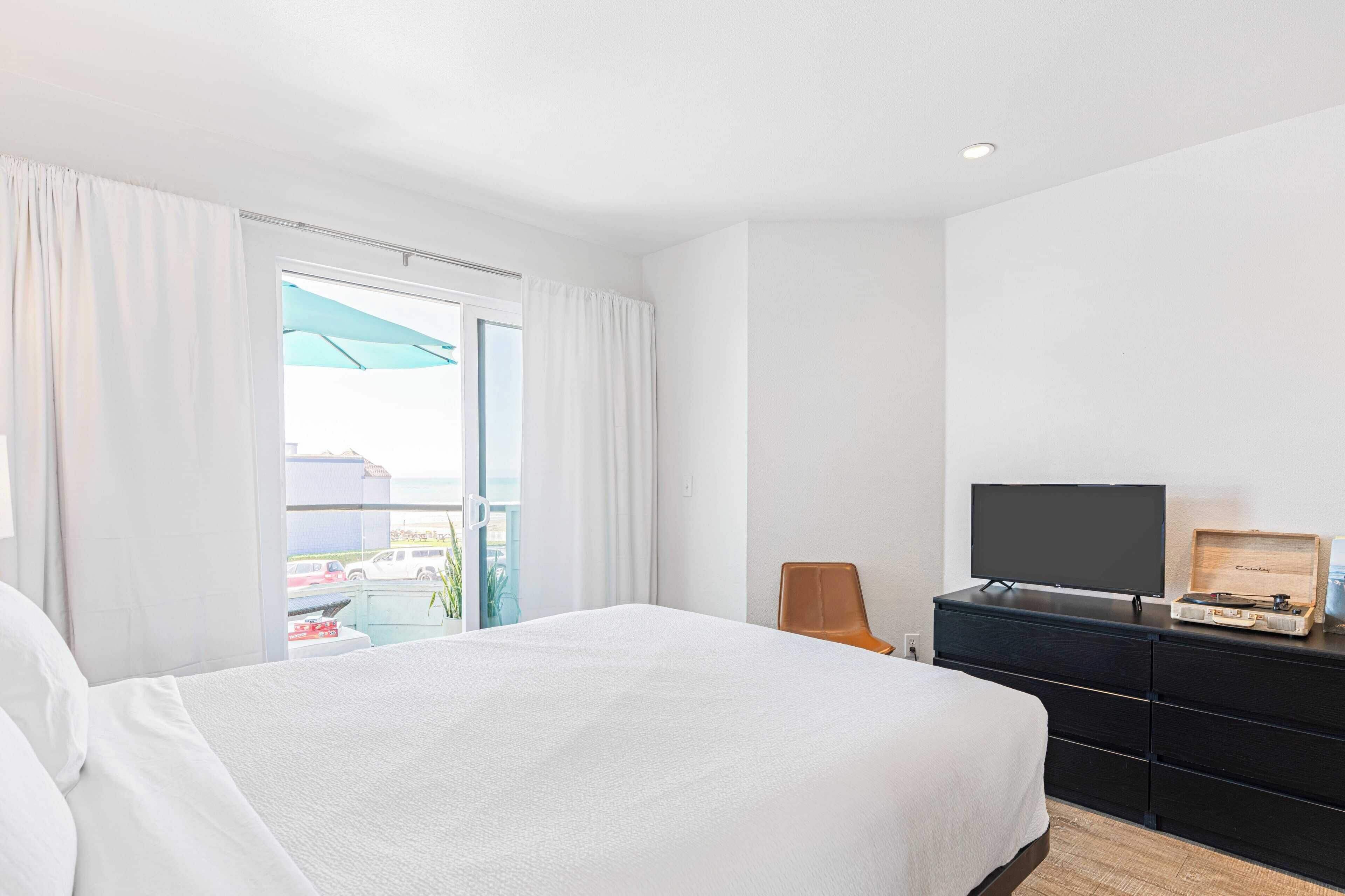 A hotel room with a large bed, a television on a dresser, and a view of the outside.