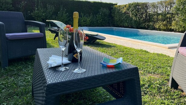 Une table installée au bord de la piscine, avec deux verres à vin, une bouteille de champagne et une petite assiette.