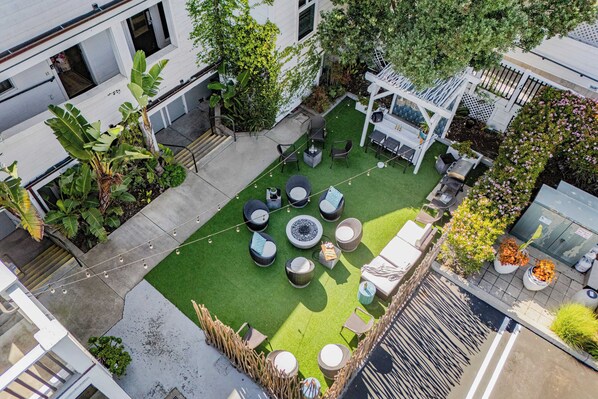 Vue aérienne d’une cour avec une pelouse artificielle verte, des sièges d’extérieur et une pergola.