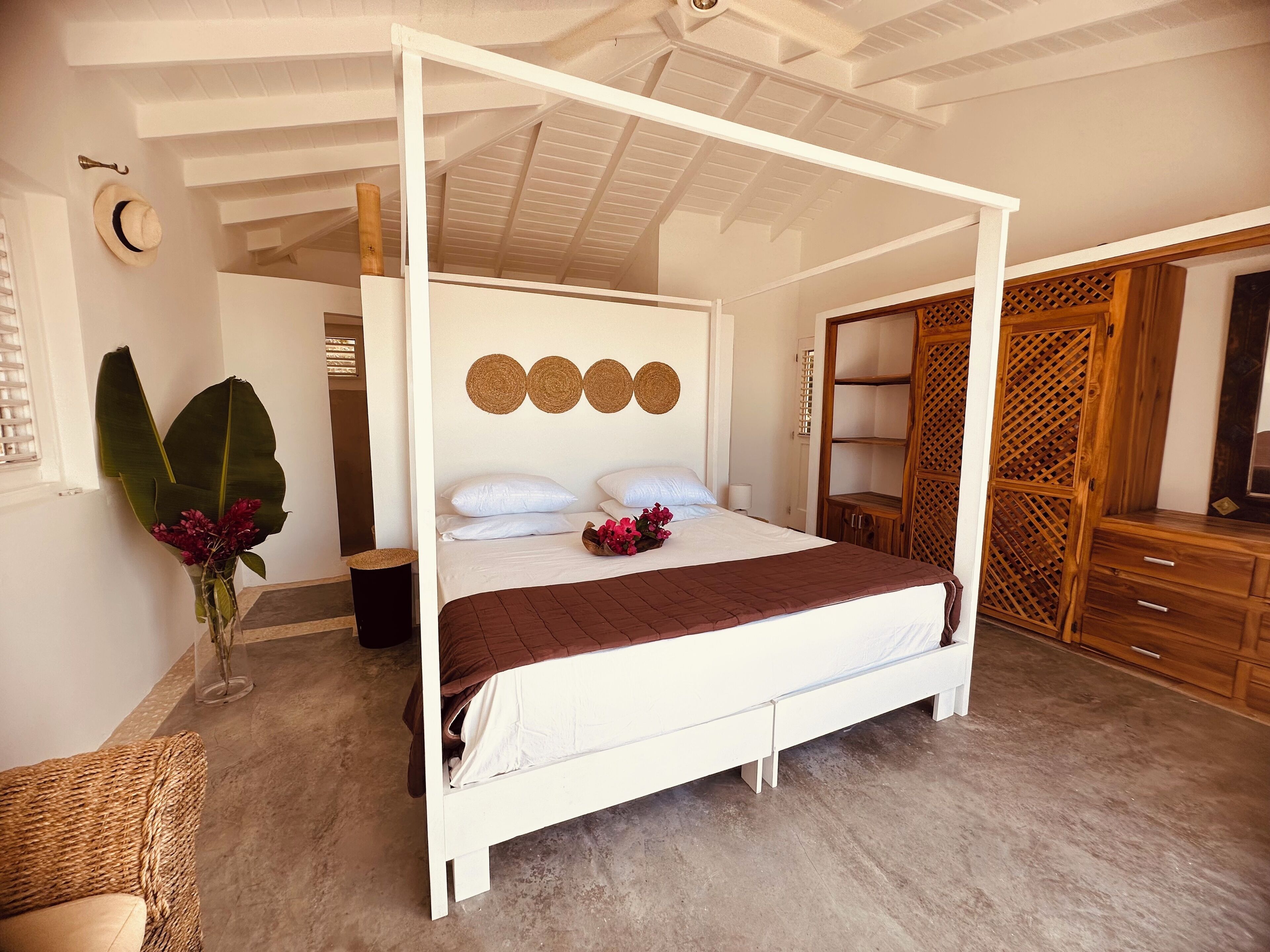 A four-poster bed with a brown bedspread, a wooden headboard, and three woven wall decorations.