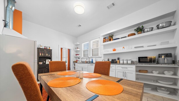 Una cocina moderna con armarios blancos, una mesa de comedor con individuales naranja y un microondas en la encimera.